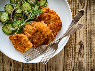 Breaded fried pork chop with sliced cucumbers and rosemary on wooden table
