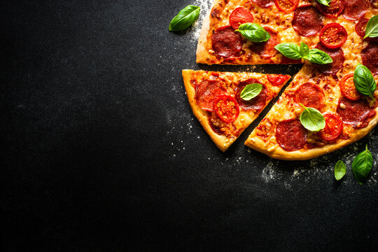 Pizza on black background. Traditional italian pizza with salami cheese, tomatoes and basil. Top view with copy space.