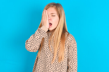 little caucasian kid girl wearing animal print sweater over blue background Yawning tired covering half face, eye and mouth with hand. Face hurts in pain.