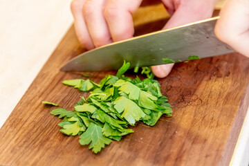 the cook cuts parsley and dill on a wooden board. cooking in a restaurant, chef's hand cutting greens on a wooden board, vegan salad with parsley,