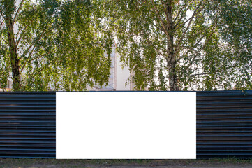 Blank white banner for advertisement on the fence of construciton site. Modern building among trees
