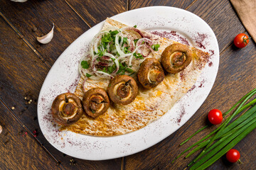 Skewers of mushrooms with sliced onion on plate on wooden table top view