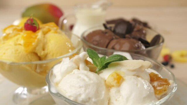 Three glass bowls filled with ice cream balls with flavors of ice cream, chocolate, mango and banana are spinning in front of the camera. Stops at yellow ice cream.