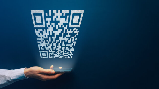 Qr code payment concept. Hand holding mobile smart phone with qr code for payment pay, scan barcode technology on dark background. Online shopping, cashless society symbol. Copy space