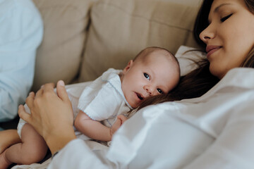 Newborn baby boy looking at the camera on top of his mother lying on the sofa