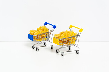 Uncooked farfalle pasta in blue and yellow shopping carts in colors of Ukrainian flag isolated on white background. Food supply crisis, price increase for wheat products, groceries shopping concept