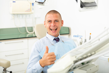 Happy male patient showing thumb up after dental treatment in clinic