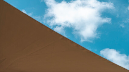 Fototapeta na wymiar Landscape cut diagonally, on one side a brown fabric parasol, on the other the blue sky dotted with fluffy clouds