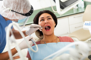 Focused man dentist in a protective mask working at the clinic treats a woman patient in a dental chair who came to see him