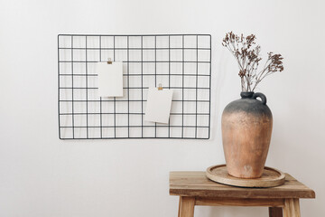 Rustic clay vase with dry hypericum bouquet on wooden table. Black metal mesh noticeboard, bulletin...