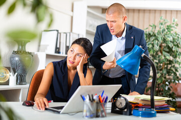 Angry boss criticizing sad frustrated employee sitting at office desk at work