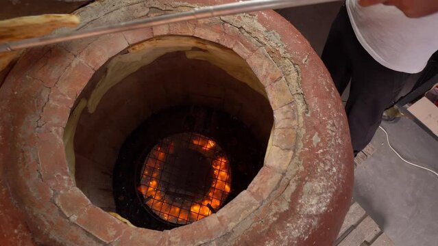 Tandoor. Inside oven, fire burns and flat bread is baked on walls. Khachapuri. Georgian cuisine. Bakery or bakery production. man with stick takes bread from wall of oven.