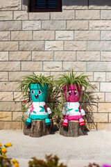 Flower pots in the shape of funny men with Chlorophytum near brick wall. Home plants