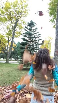 Throw Your Hands Up in the Air it's Fall!  Middle age caucasian female throws autumn leaves up in the air in slow motion. Wearing hat and vest with back to camera. 