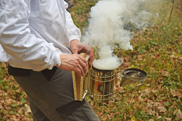 L'apiculteur nettoie les cadres de ses ruches. Il enfume les abeilles pour que la fumée les calme.