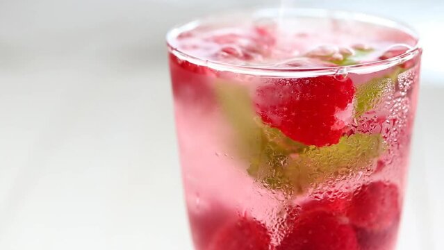 Raspberry cocktail.Splashes and drops of a Summer drink. glass with raspberry pink drink.raspberries in a glass with water, berries and raspberry leaves on a white wooden table. 