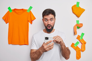 Shocked bearded man stares at smartphone screen surprised to read amazing news or someone tried to...