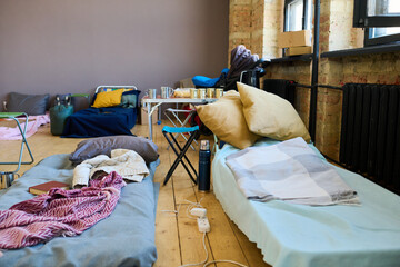 Two sleeping places of refugees with mattresses done with blankets or plaids in spacious room prepared for temporarily homeless people - obrazy, fototapety, plakaty