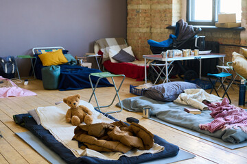 Part of spacious room with sleeping places on wooden floor for refugees or temporarily homeless people because of war or cataclysm - obrazy, fototapety, plakaty