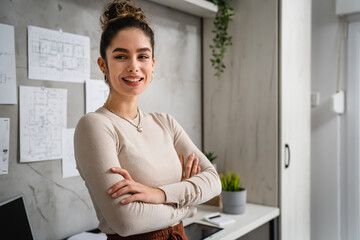 One confident woman female entrepreneur or student standing in front of the desk ar home or work looking to the camera with arms crossed real people copy space half length happy smile