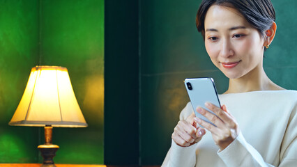 暗い部屋でスマホを使う女性 © metamorworks
