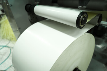 Roller of white printing paper for self-adhesive label on the shaft of the die-cutting machine in...