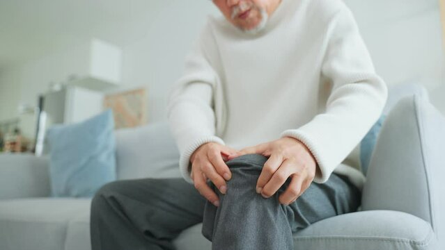 Asian Senior elderly disabled man sit on sofa suffer from injured leg.