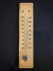 Analogue wooden thermometer with red measuring liquid on black background