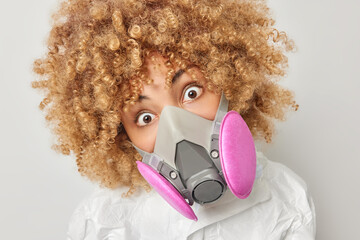 Protection against viruses. Startled shocked curly haired young woman stares bugged eyes wears gas...
