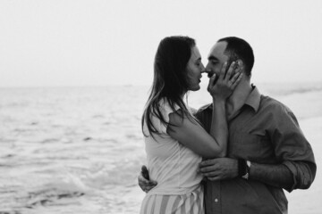 Black and white photo. Young romantic couple dancing turning around by sea. Seascape at sunset with beautiful sky. Romantic couple on the beach at golden sunset. Lover couple having fun on beach.