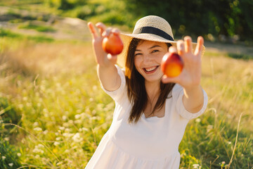 Happy carefree summer girl in outdoor field with orange peach fruit. Young woman eats peach. Summer...