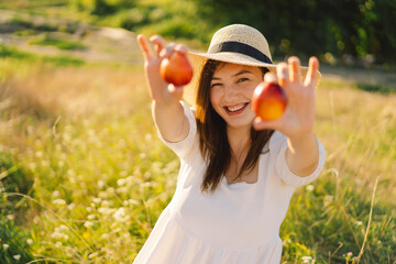 Happy carefree summer girl in outdoor field with orange peach fruit. Young woman eats peach. Summer picnic setting.