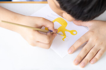 Close up of cute Asian little boy drawing and painting his imagination monster character on white...