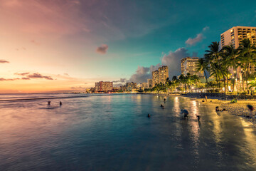 Fototapeta premium Night panorama of Waikiki Beach and building by the shore line with palm trees in Honolulu, Hawaii. Sunset light