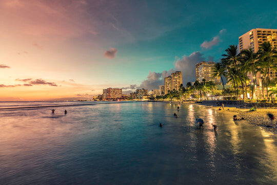 Night Panorama Of Waikiki Beach And Building By The Shore Line With Palm Trees In Honolulu, Hawaii. Sunset Light