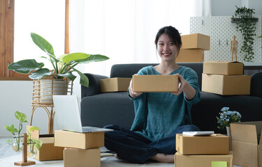 Fototapeta na wymiar Happy young asian woman startup small business freelance holding parcel box and computer laptop and sitting on floor, Online marketing packing box delivery concept