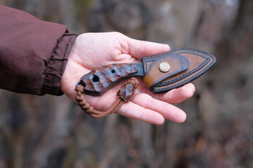 - Exclusive handmade knife in hands of man on background of big tree.
