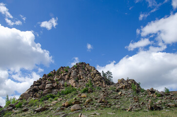 A rock with large stones against the background of a blue sky. A summer day.