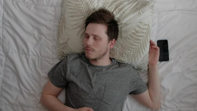 High angle view of an overslept caucasian male wake up getting out of bed in shock because he is late for work in the morning at home.