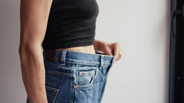 Diet concept and weight loss. Woman in oversize jeans on pastel white background