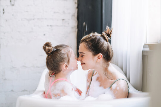 Young mother woman and little tween girl daughter having fun in bath with foam at home