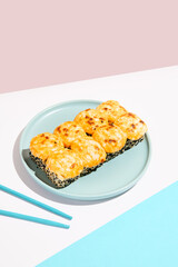 Hot maki roll with cheese and sesame on coloured background. Baked sushi roll with salmon inside, sesame outside, cheese topped. Maki sushi in minimal style. Japanese menu concept.