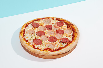 Italian pizza with ham and salami on coloured background. Meat pizza with ham and pepperoni in minimal style on light blue color. American pizza delivery concept with color backdrop