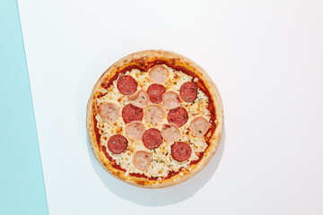 Italian pizza with ham and salami on coloured background. Meat pizza with ham and pepperoni in minimal style on light blue color. American pizza delivery concept with color backdrop