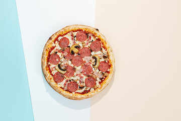Italian pizza with salami, bacon and mushroom on coloured background. Meat pizza with salami and bacon in minimal style on blue and orange color. American pizza delivery concept with color backdrop