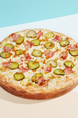 Italian pizza with bacon, pickled cucumber and crispy onion on coloured background. Homemade pizza in minimal style on blue and orange color. American pizza delivery concept with color backdrop.