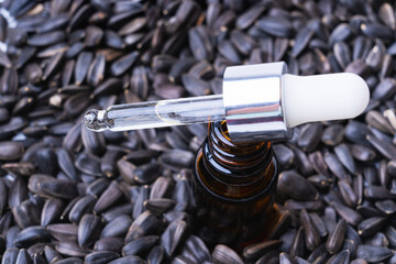 A pipette and a bottle of essential oil stands on sunflower seeds, top view