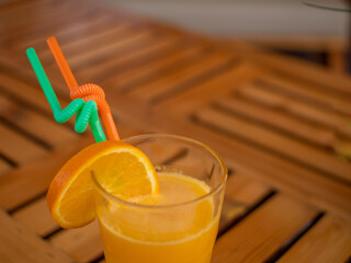 A glass of orange juice with an orange slice and two straw.