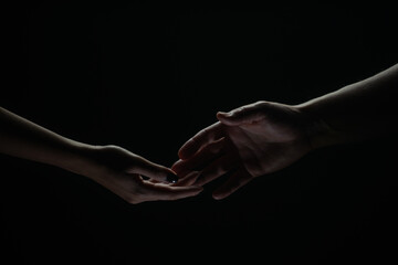 Two hands reaching toward. Helping hand outstretched for salvation on isolated black background. Close up of man and woman hand touch with fingers. Man and woman holding hands.