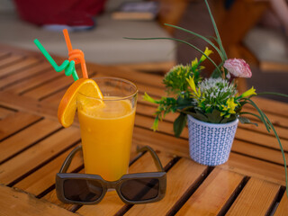 Composition of a glass of orange juice, sunglasses and of beautiful flowers.